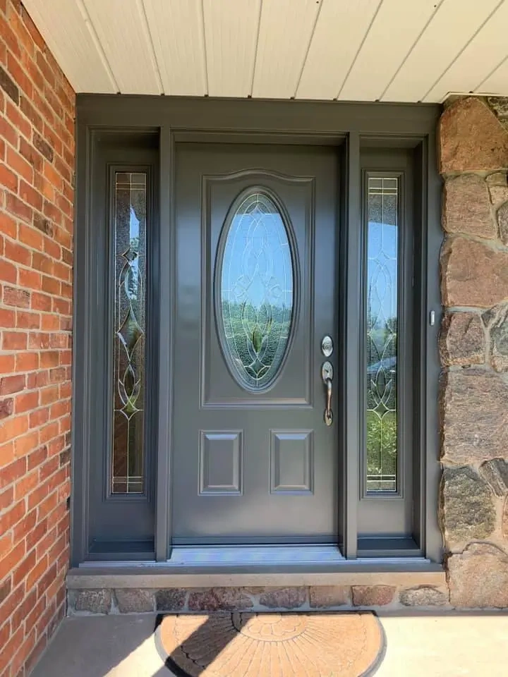 Grey Dorplex entry door with oval decorative glass and matching sidelites installed on a brick and stone home exterior