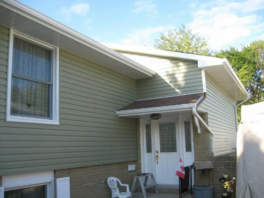 Completed white eavestrough, fascia, soffit and downpipe installation on a green-sided home